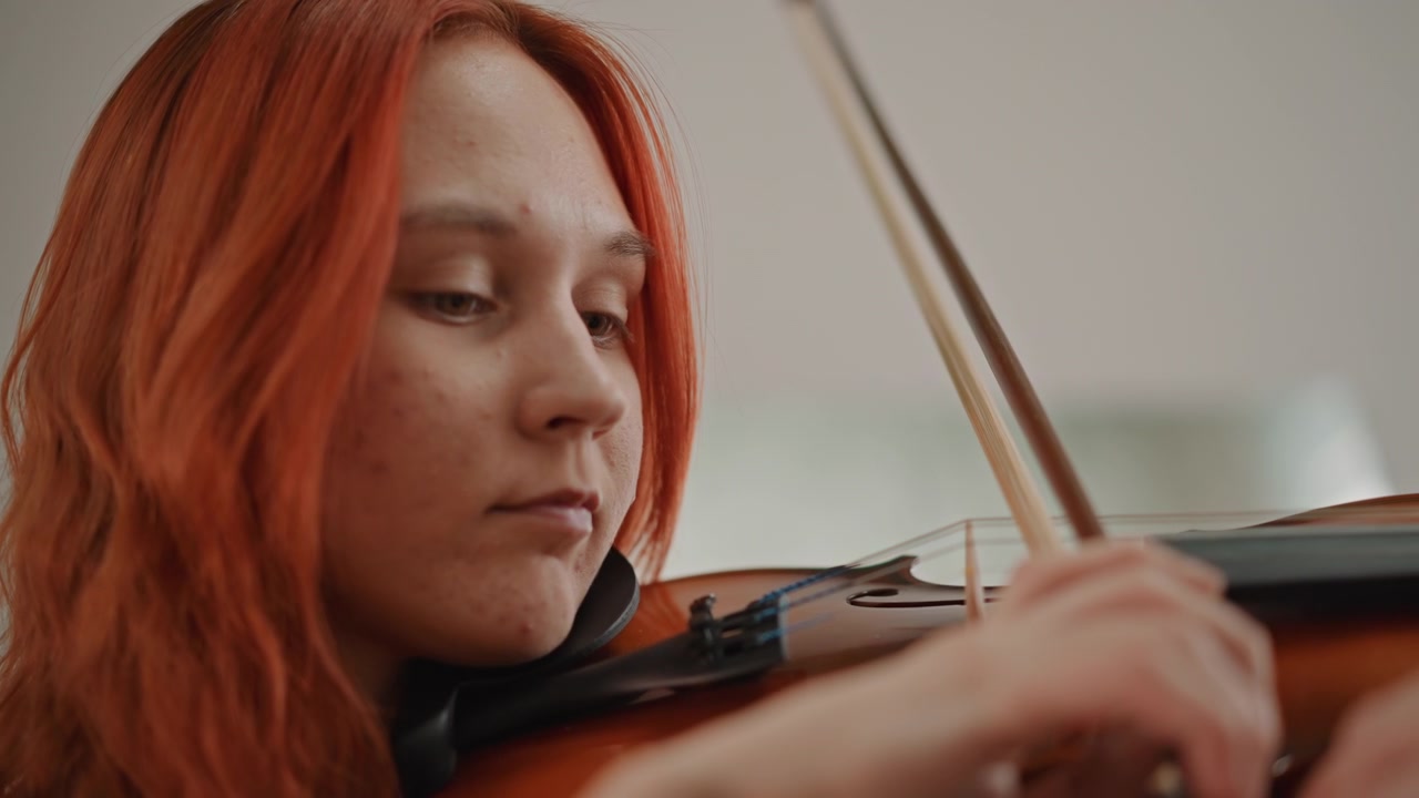 Redhaired violinist practicing focused solo phrases, closeup portrait showing intense concentration, delicate fingering and bow control, rich warm tone in quiet studio classroom