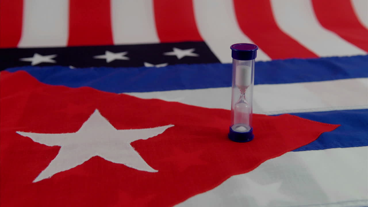 실행 모래 시계 아래에 미국과 쿠바 국기가 놓여 있습니다.