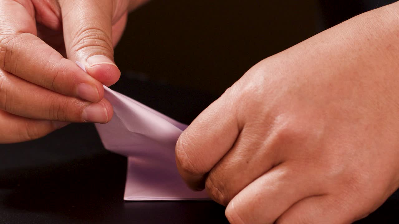 Adult hands carefully fold white paper into an origami boat, close-up, warm studio lighting