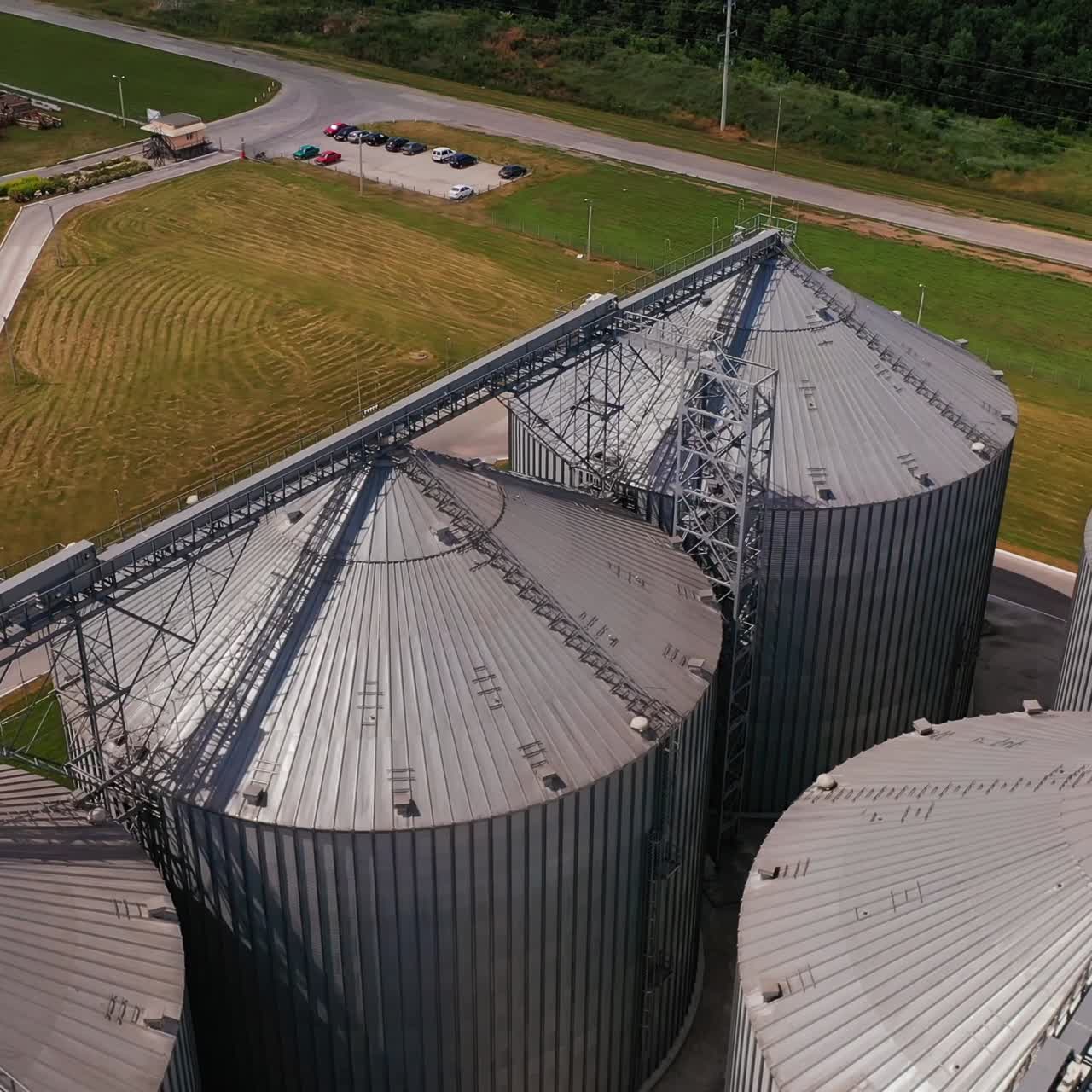 Large steel storage for agricultural harvest. Flight above huge silo tanks complex. Beautiful greenery at the backdrop