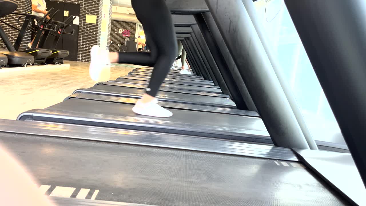 una giovane ragazza può essere vista in una vista ampia, impegnata in una corsa lenta sul tapis roulant, concentrandosi sul suo viaggio di fitness e sull'allenamento di resistenza