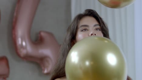 a female fashion model looking at bouncing golden balloons with a big smile