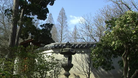 Puesto-De-Farolillos-Japoneses-Frente-A-Una-Pared-Con-Techo-De-Tejas-En-Un-Jardín-Japonés-De-Vista-Prestada-O-&quot;shakkei&quot;