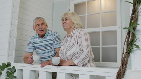 senior elderly couple drinking coffee, embracing in porch at home during coronavirus quarantine