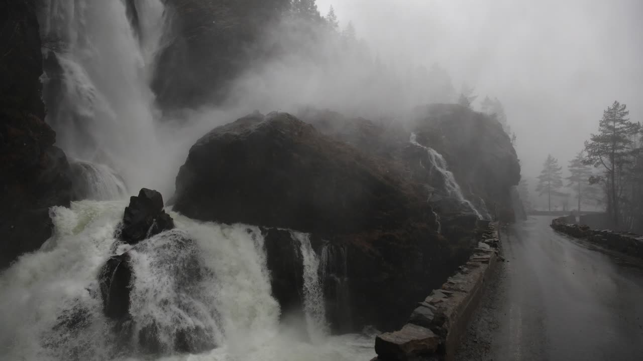 Heavy rain and flooding as massive waterfall crashes beneath road bridge. Everything is dark and wet during extreme weather and storm runoff