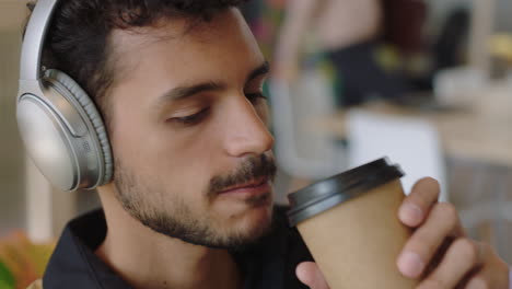 cerca joven hispano usando computadora portátil navegando mensajes en línea compartiendo comunicación en red estudiante bebiendo café disfrutando escuchando música en una oficina moderna