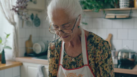 elderly woman in apron reading recipe book in home kitchen