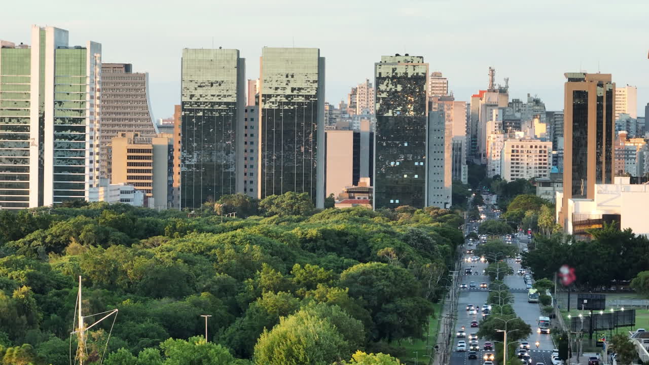 Paralaxe de teleobjetiva revela o horizonte de Porto Alegre acima do Parque Marinha e do tráfego da Avenida Borges de Medeiros ao pôr do sol, 4K50.