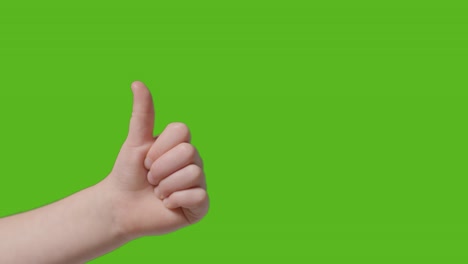 close up of child giving thumbs up gesture to camera against green screen 1