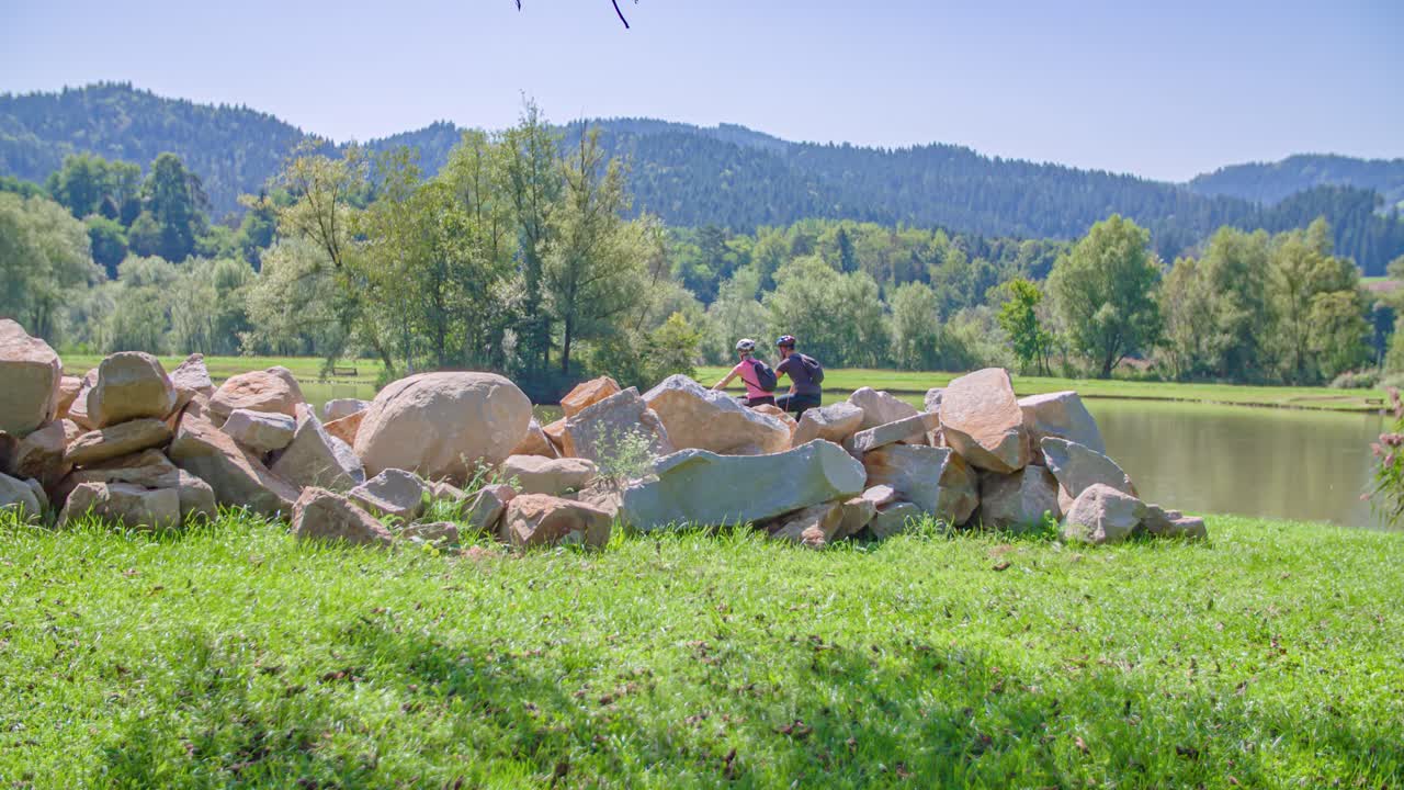 Two young travelers riding bikes alongside a beautiful lake in Slovenia. Slow motion