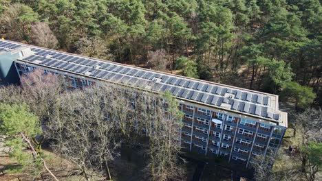 Cinematic-aerial-of-old-apartment-building-with-photovoltaic-solar-panels-on-rooftop-on-a-sunny-day