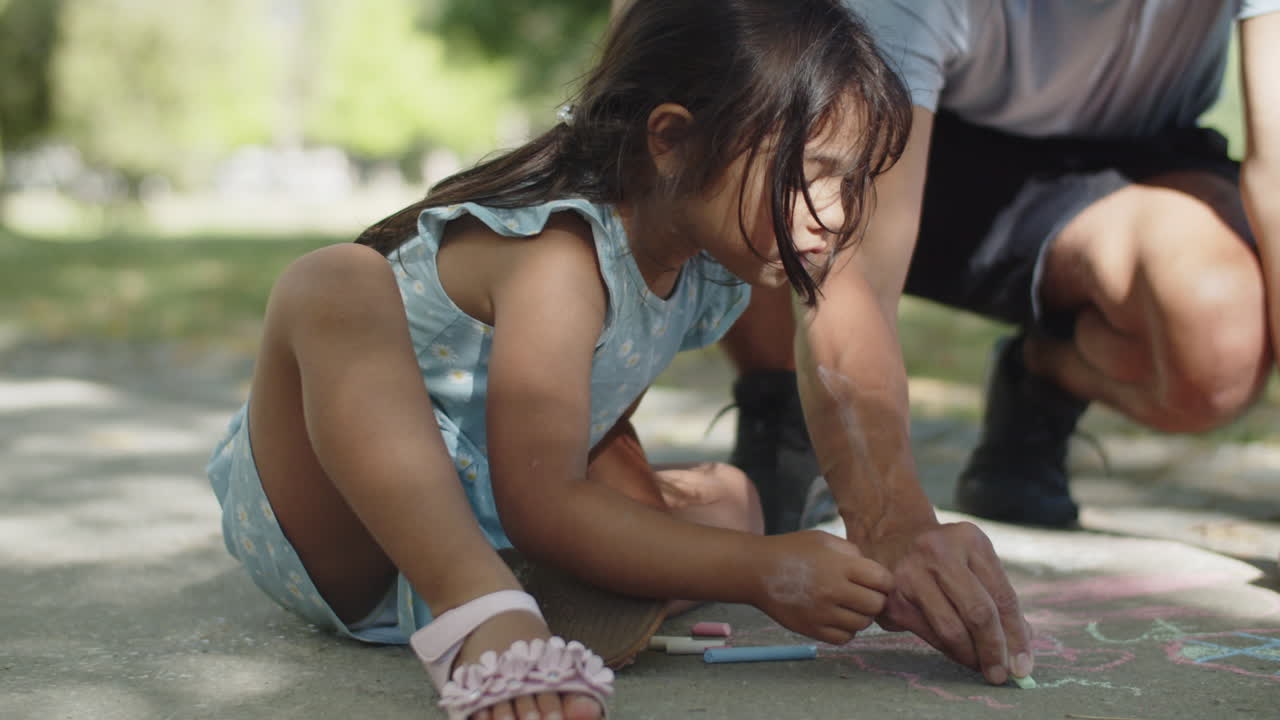 niña asiática feliz y su padre dibujando con tizas de colores