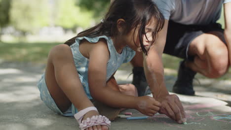 happy asian girl and her father drawing with colorful chalks