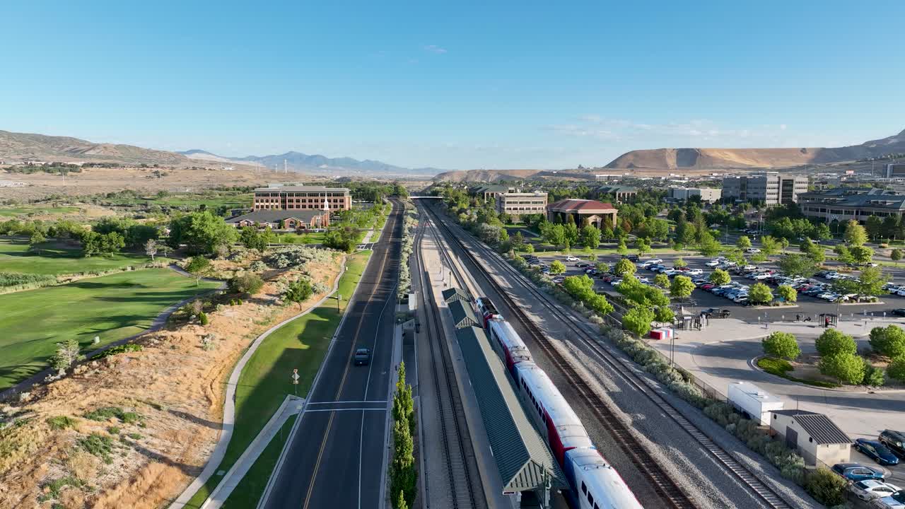 FrontRunner light rail commuter passenger train leaving Lehi Station in towards Provo - pullback aerial reveal on a sunny morning