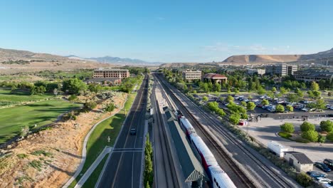 frontrunner light rail commuter passenger train leaving lehi station in towards provo - pullback aerial reveal on a sunny morning