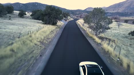 cinematic blue hour car chase in snow basin utah white car driving fast down a mountain valley road - aerial chase follow