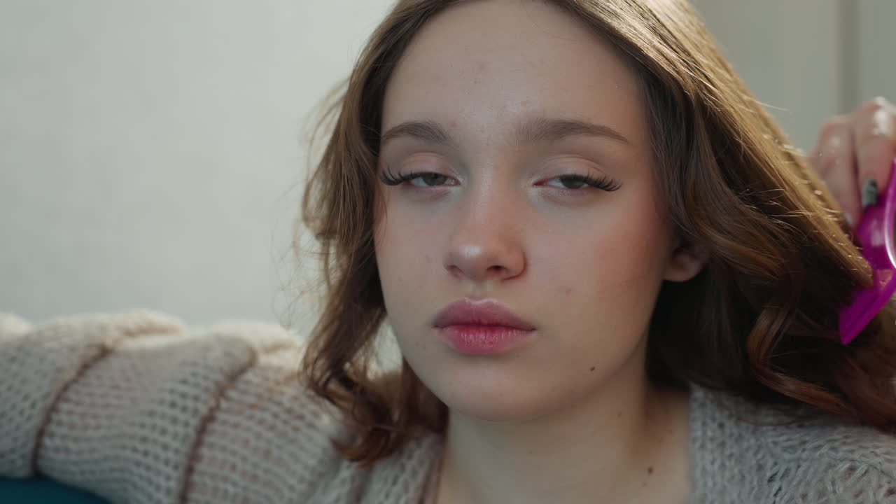 Young Caucasian Woman On Sofa Brushing Hair, Quiet Living Room, Soft Natural Light, Pensive Expression, Hands Gently Tousling Wavy Brown Hair, Cozy Knit Sweater, Domestic Intimate Beauty Study, Slow