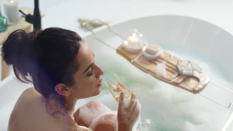 caucasian woman relaxing with glass of white wine in bathtub