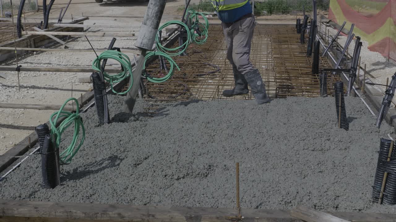 Close-up of worker pouring concrete on foundation using hose, with visible cables and site elements - Israel