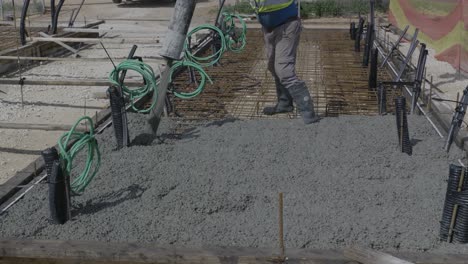 close-up of worker pouring concrete on foundation using hose, with visible cables and site elements - israel