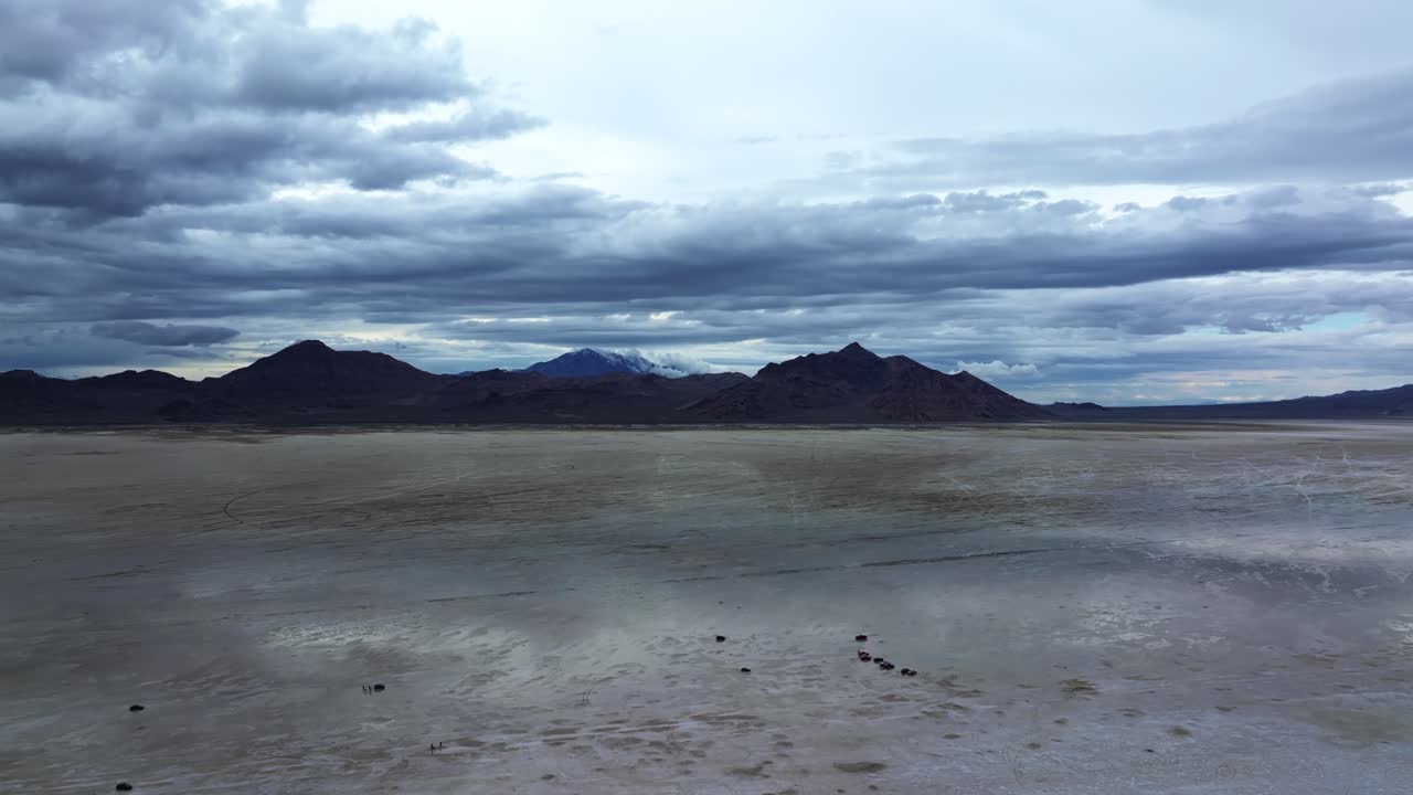 Extreme wide aerial drone tilt down shot revealing cars drifting on the Bonneville Salt Flats in Utah near Wendover Nevada on a stormy spring evening with patches of wet and dry spots from rain