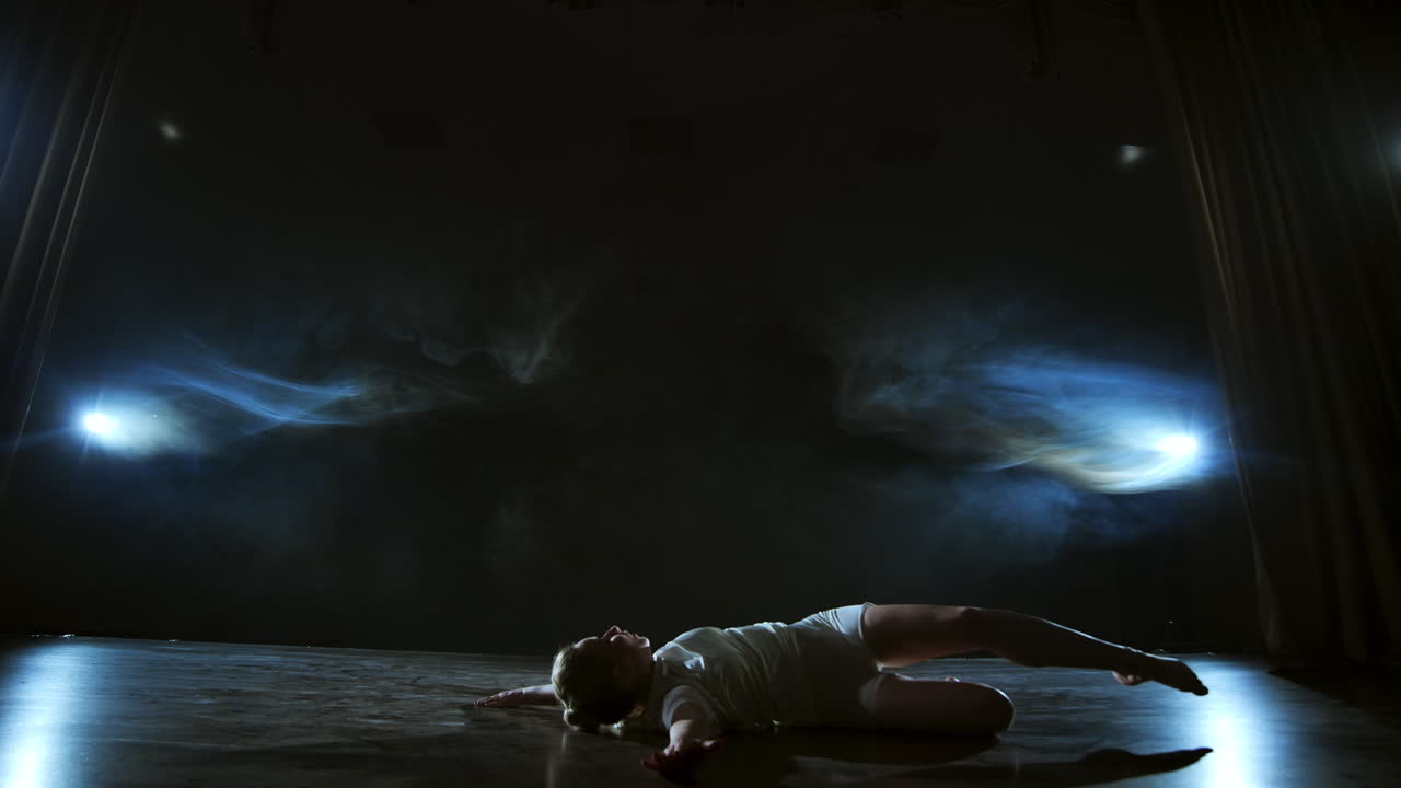 Slow motion: Modern ballet dancing woman barefoot lying on the floor doing spins and pirouettes and somersaults.