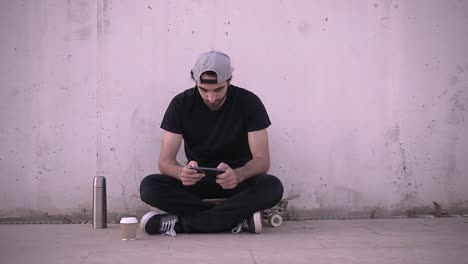 young man relaxing outdoors with smartphone and skateboard