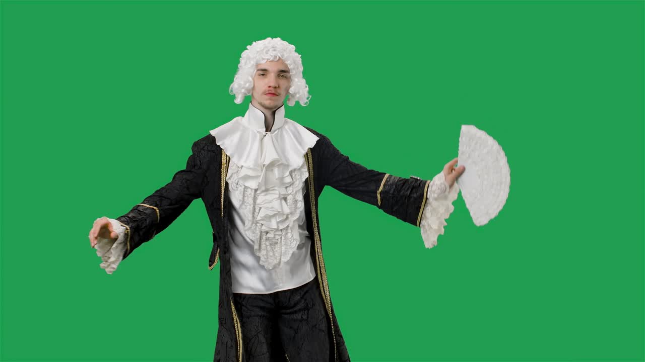 retrato de un caballero cortesano en traje vintage histórico negro y peluca blanca, agitando un abanico y una reverencia. joven posando en el estudio con fondo de pantalla verde. cámara lenta