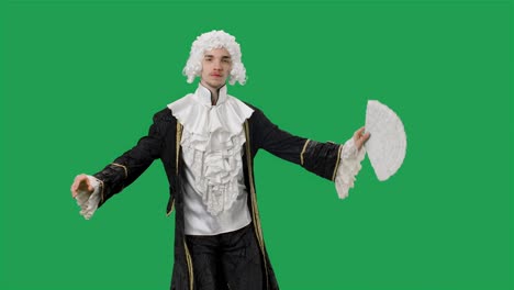 portret van een hofman in een zwart historisch vintage pak en een witte pruik, met een waaier en een buiging. jonge man die poseert in een studio met een groene achtergrond. slow motion