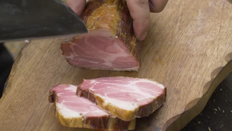 chef cutting a piece of fatty pork ham on a handmade wood chopper. the knife is made by hand and is called almazan. it is very sharp and has a unique design