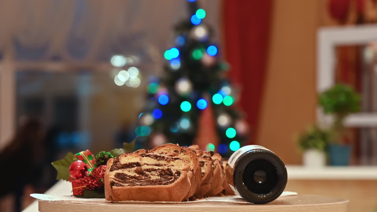 Cutted baked roll with stuffing on a plate, wine and decoration near it, Christmas tree on the background