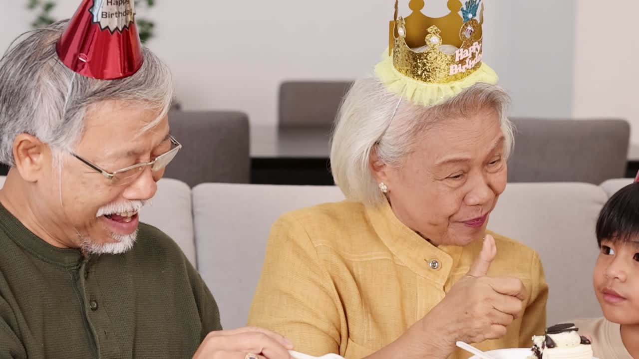 楽しいお祝いの席で、パーティーハットをかぶりケーキを食べる多世代のアジア人家族。