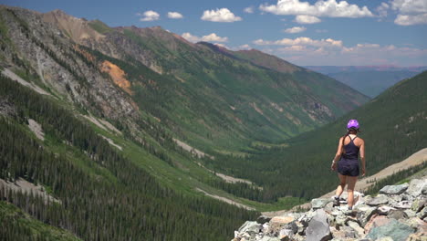 young female hiker with helmet walking on rocky boulder with stunning view of green valley in rocky mountains, colorado usa