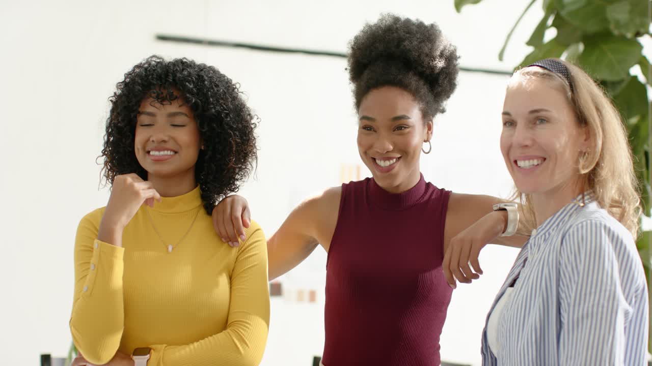 Compañeras de trabajo diversas con tops posando en estudio, respondiendo a una señal fuera de cámara, uniendo los hombros