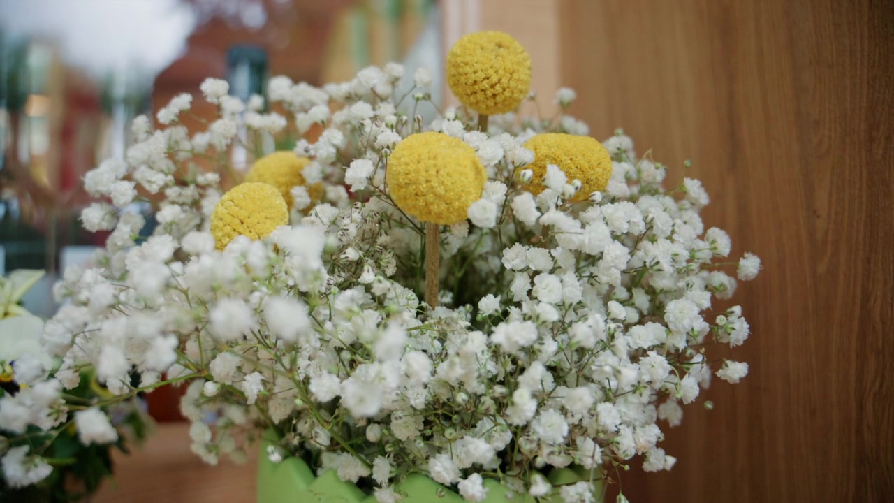 Close up of a floral arrangement featuring delicate white blossoms and yellow flowers in a decorative vase