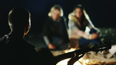 the company of friends relaxing by the fire a man plays guitar