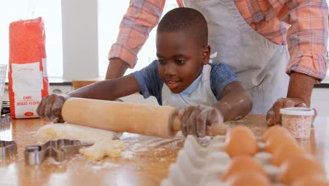 Front-view-of-little-black-son-rolling-dough-with-rolling-pin-in-kitchen-of-comfortable-home-4k