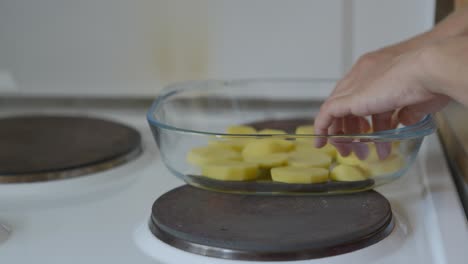 Close-up-shot-of-a-woman-placing-potatoes-in-a-glass-baking-tray,-in-a-small-kitchen-during-summer-midday