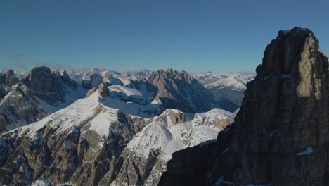 aerial pull back view from snowy mountain alps terrain to reveal sunlit tre cime stunning peaks