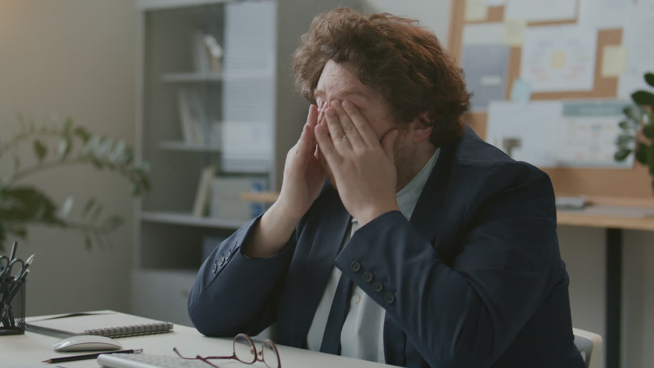 Uomo d'affari stanco che si strofina il viso mentre lavora al computer alla scrivania dell'ufficio