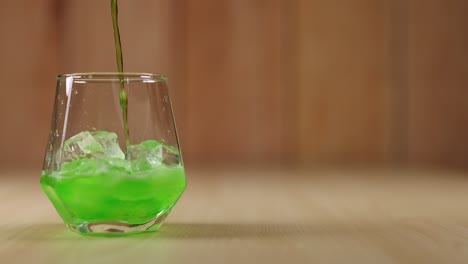 green liquid poured into glass with ice