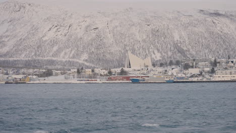 wide shot showing calm water of fiord and snow covered mountains and famous arctic cathedral in background
