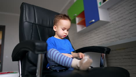 baby sitting in big black chair looks at phone. low angle view on the toddler using a gadget.