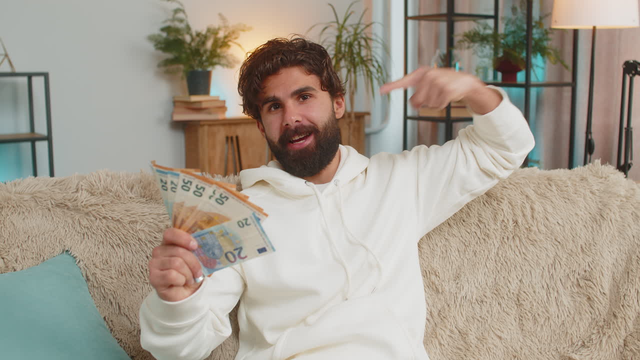 Succesvolle, rijke, jonge Spaanse man zit met een waaier van eurobiljetten op een bank thuis