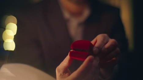 enamoured guy proposing engagement opening gold ring box at night hotel closeup