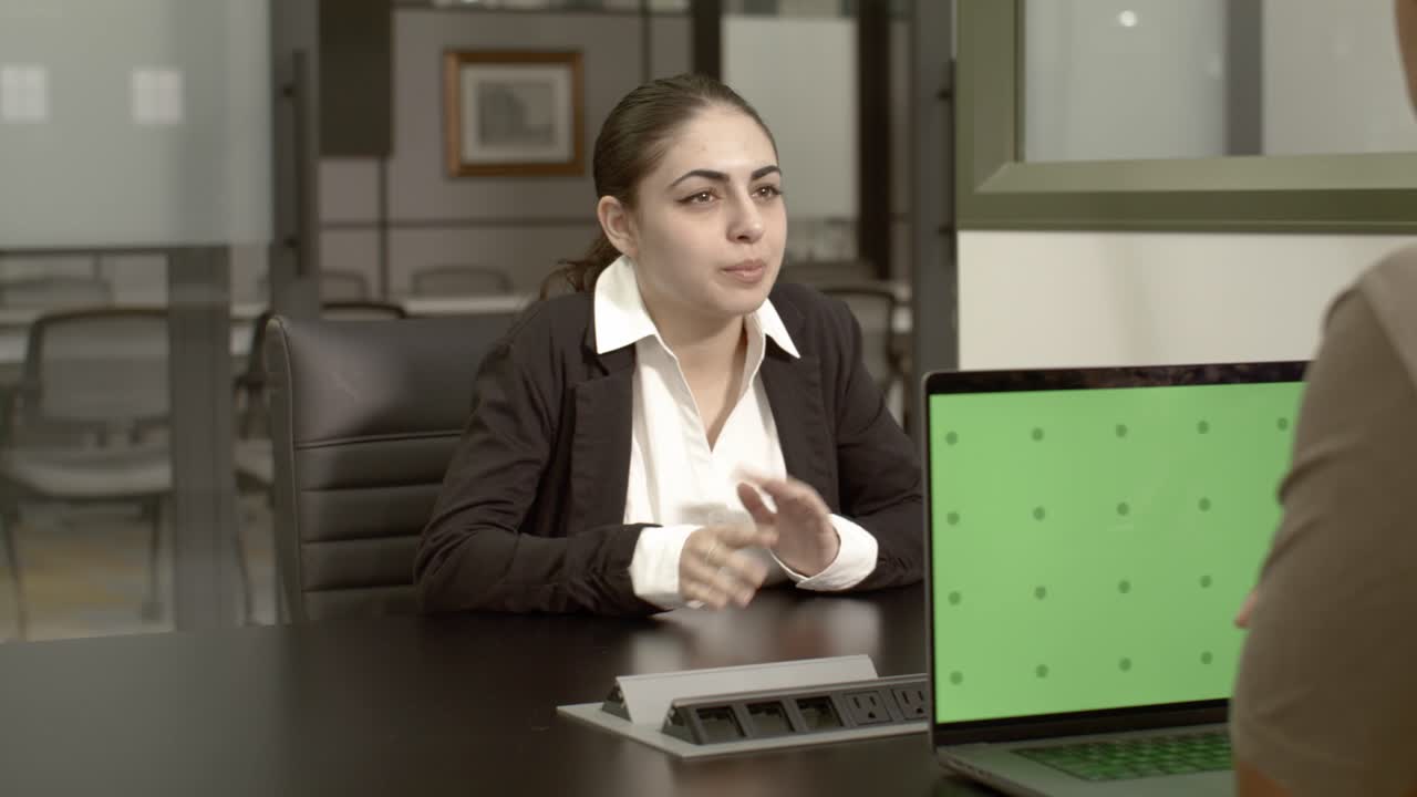 una mujer árabe-estadounidense de unos 20 años en una oficina hablando con un hombre afroamericano de 20 años.