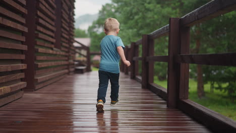 little blond boy runs turning back along wet veranda deck