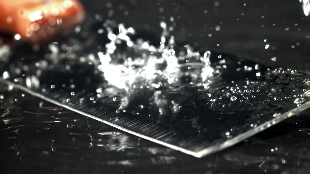 Gocce d'acqua che schizzano su una superficie scura e riflettente al rallentatore