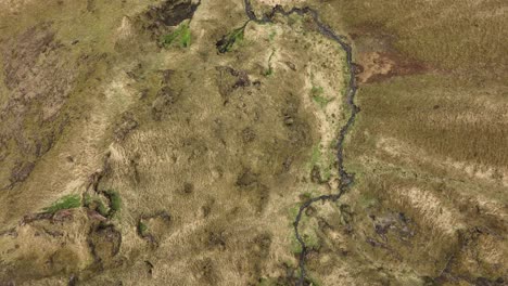 aerial shot of barren, textured grasslands in brókarjökull, iceland, with a narrow stream winding through the rugged and rocky terrain