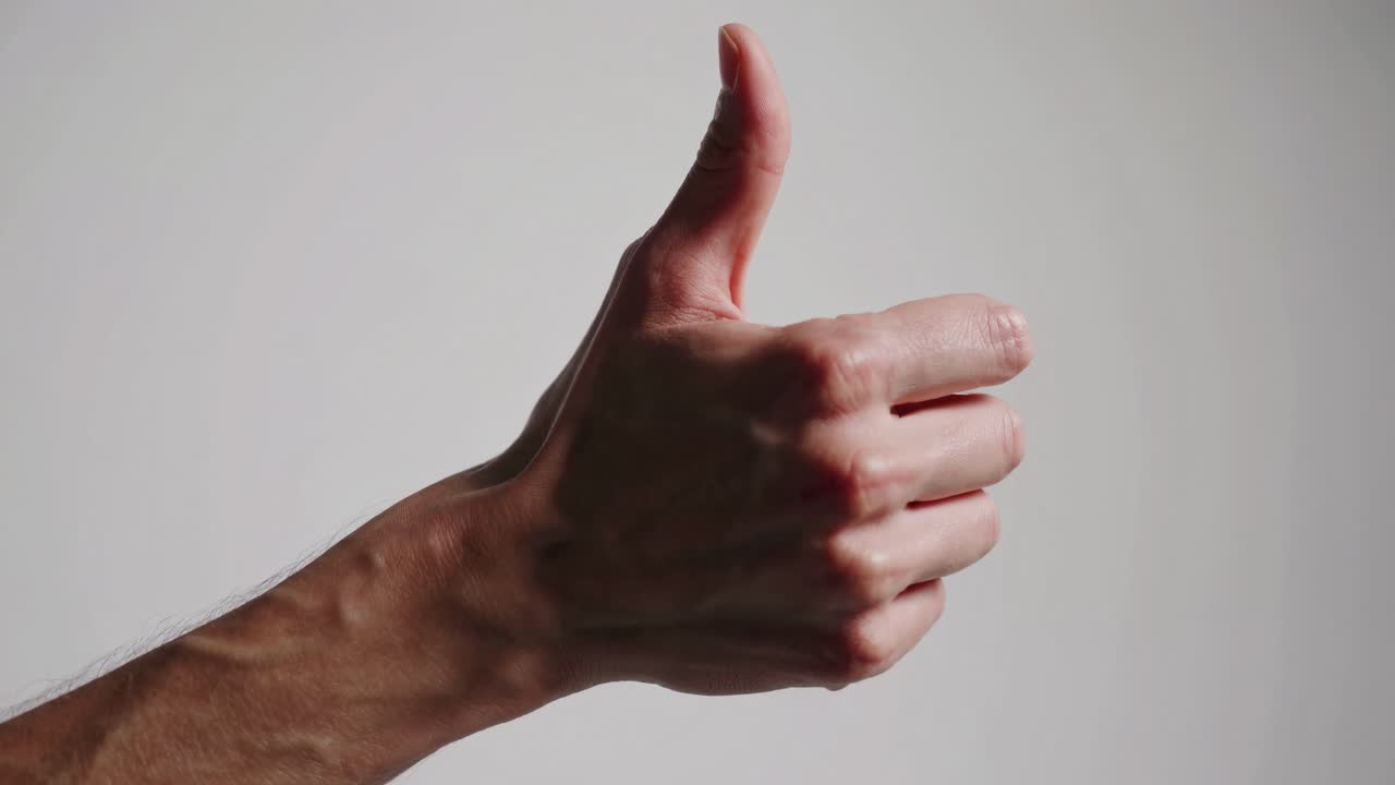 Toma de vídeo en primer plano de una mano haciendo un pulgar hacia arriba sobre un fondo neutro, grabada desde un lateral